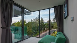 A modern room with a green sofa, large sliding glass doors, and a view of a road and greenery. - Twin Sands by Lofty (Patong)