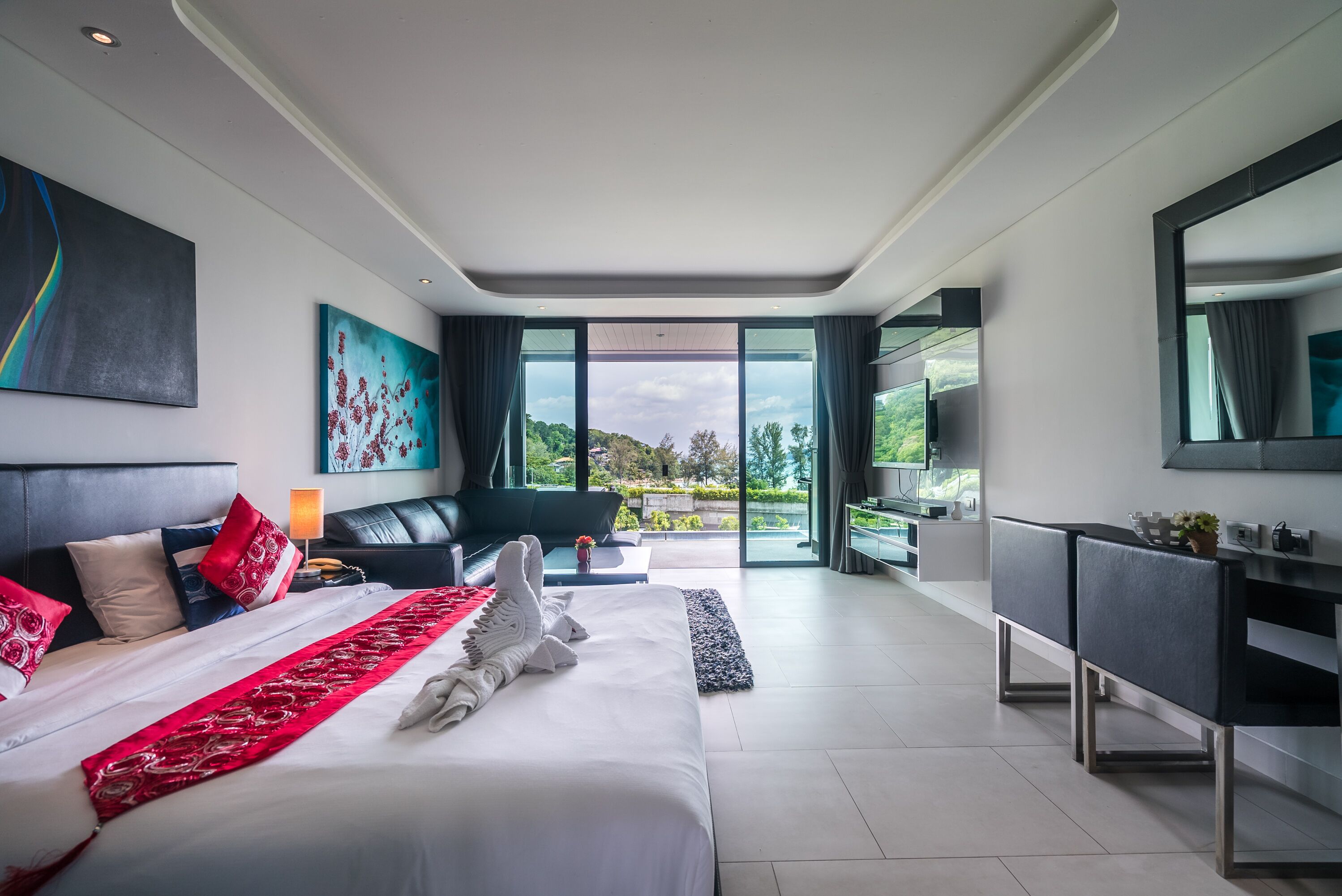 A modern hotel room with a large bed, a sofa, a desk, and a view of the outdoors.