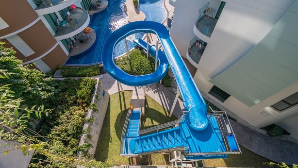 A multi-level pool area with a blue water slide, surrounded by balconies and lounge areas. - Twin Sands by Lofty (Patong)