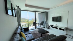 A modern living room with a leather sofa, a flat-screen TV, and a balcony with a view of the city. - Twin Sands by Lofty (Patong)