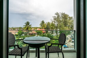 A balcony with a round table and two wicker chairs, overlooking a residential area with houses and palm trees. - Oceanstone Resort by Lofty (Choeng Thale)