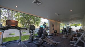 Ein Fitnessstudio mit Cardiogeräten, Gewichtecken und einem großen Fenster mit Blick auf Grünflächen.