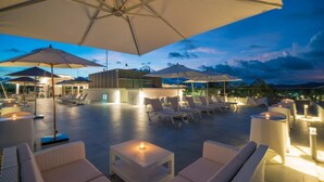 Eine Dachterrasse mit Sitzgelegenheiten im Freien, Sonnenschirmen und einem Pool.