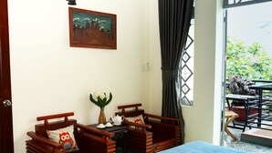 A room with a bed, a wooden table with a vase and teapot, two wooden chairs, and a painting on the wall. - PT House (Ho Chi Minh City)