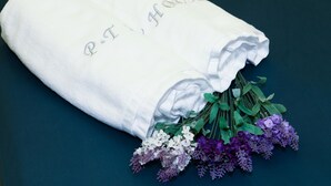 A folded white towel with embroidered text and a bouquet of purple and white flowers on a dark surface. - PT House (Ho Chi Minh City)