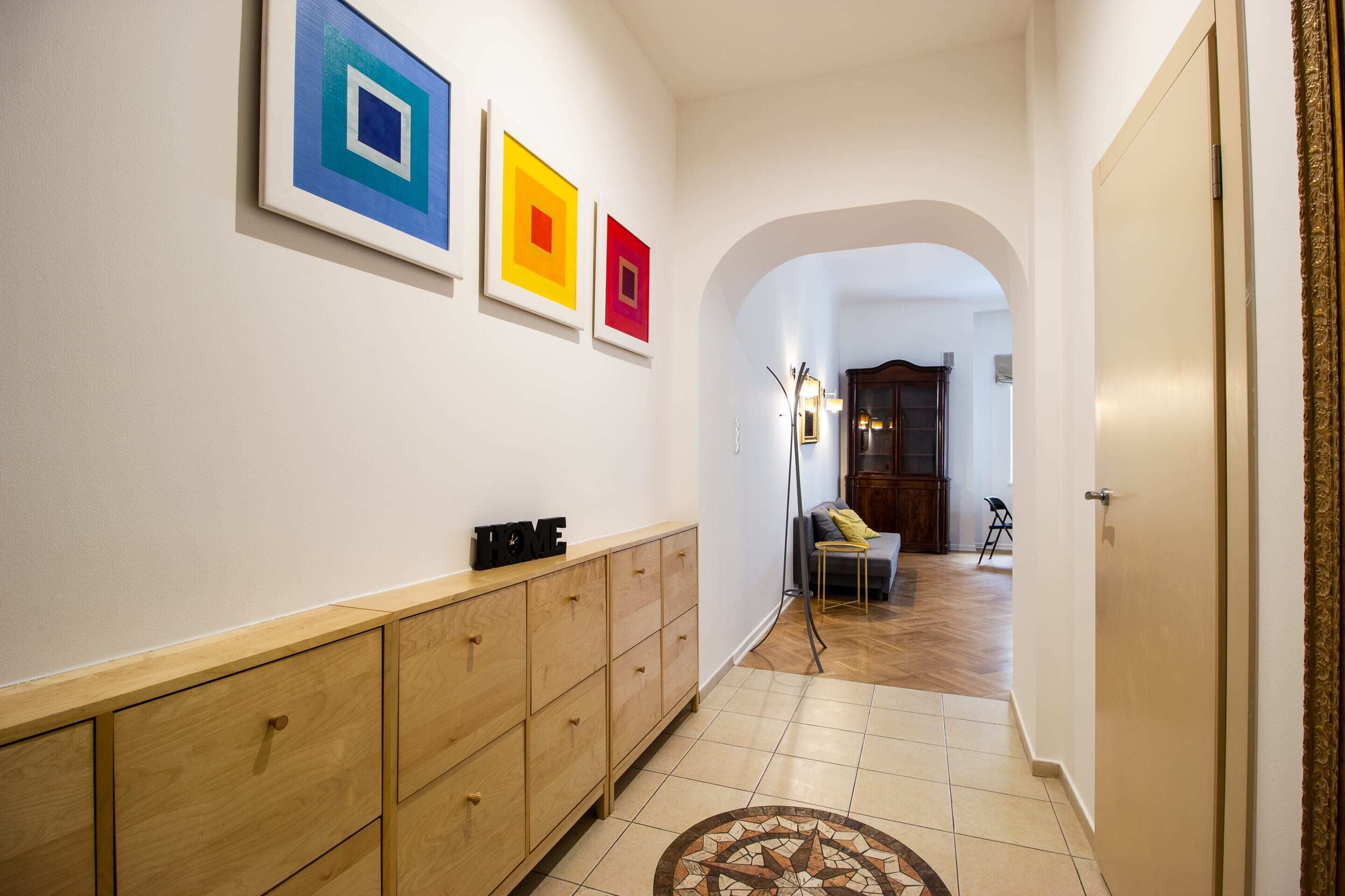 Un pasillo con un aparador de madera, una lámpara de pie y obras de arte enmarcadas en la pared.