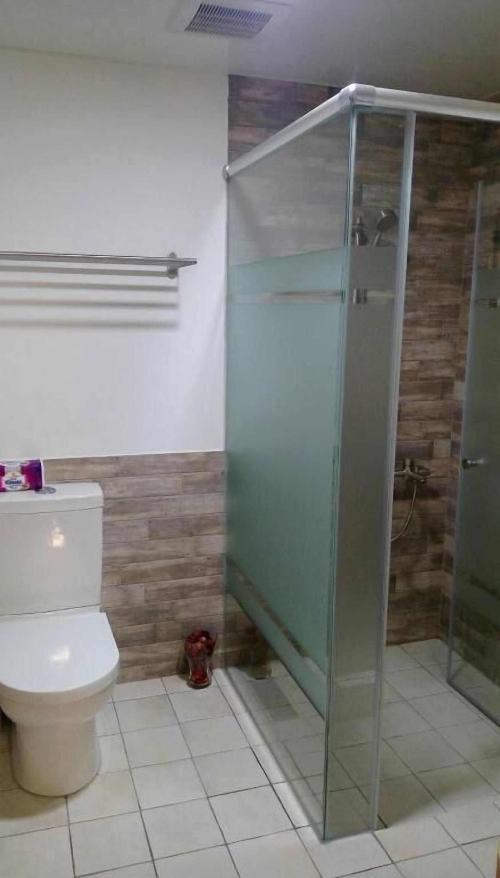 Casa de banho com sanita, cabine de duche em vidro e um porta-toalhas.