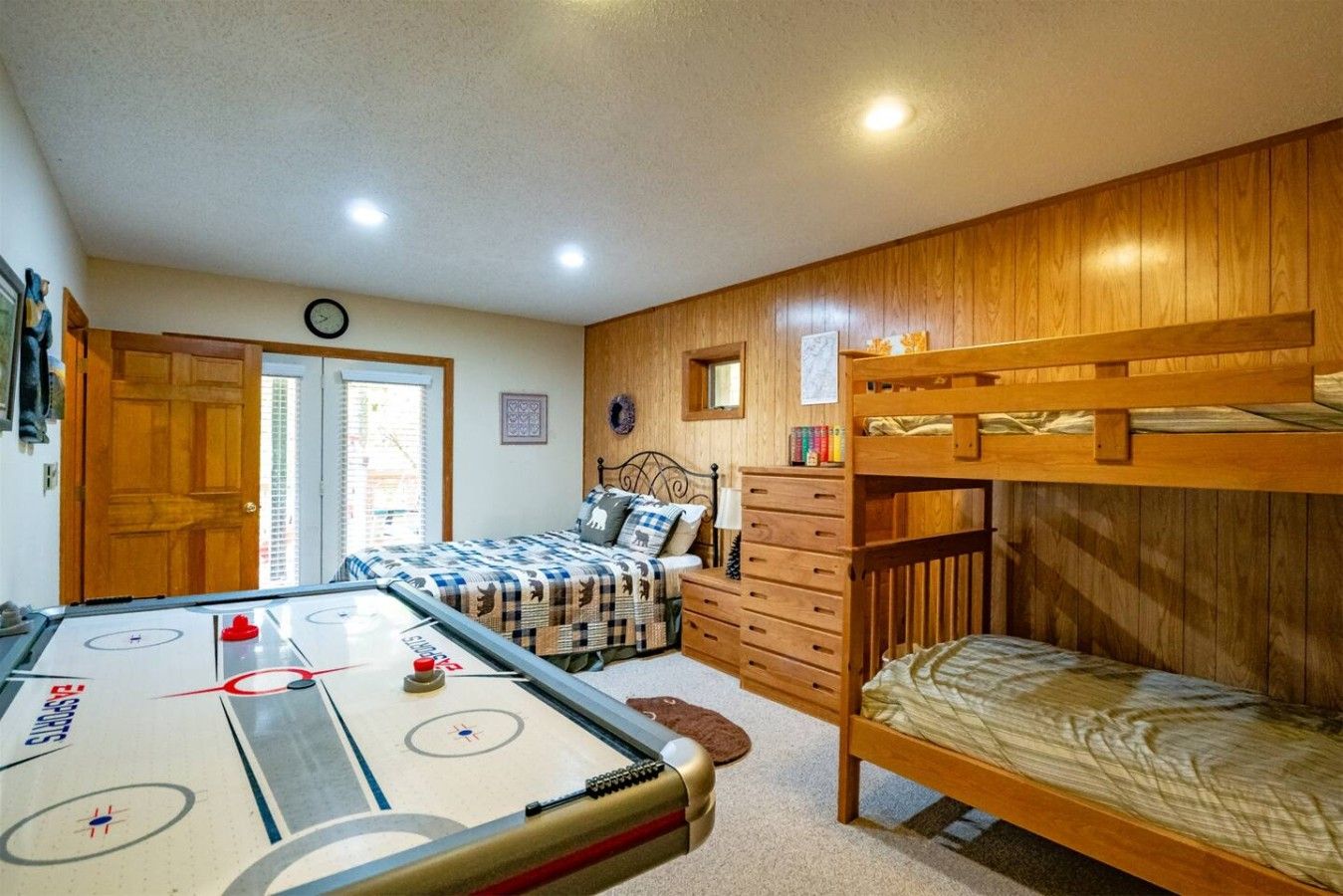Una habitación con mesa de billar, literas, una cama, un aparador y una puerta.