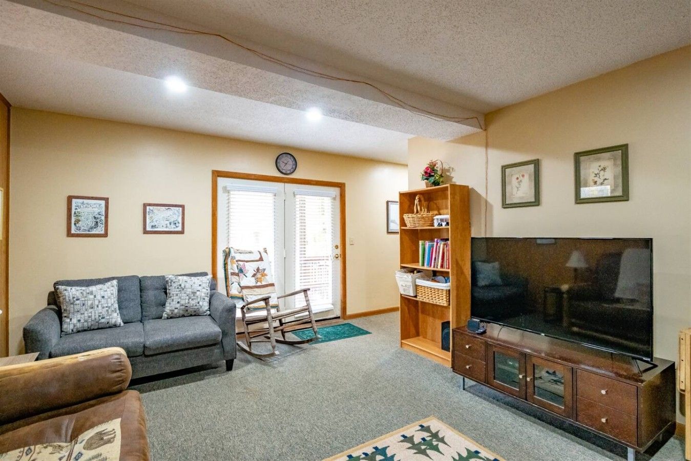 Una sala de estar con un sofá, una televisión, una estantería y un sillón mecedora.