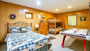 Un dormitorio con una cama nido, una cama individual con colcha estampada, un escritorio con computadora y un estante en la pared con libros.