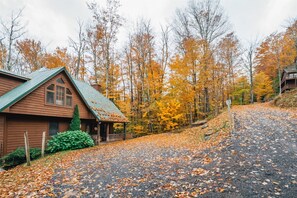 Un chalet rustique avec un toit végétalisé, entouré d’un feuillage automnal et bordé d’une allée de gravier.