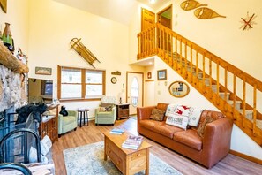 A cozy living room with a brown leather sofa, a wooden coffee table, and a staircase leading to an upper level.