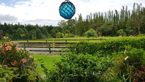 Un jardín con terraza de madera, abundante vegetación y un objeto esférico azul colgando.