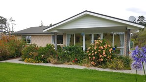 Una casa de dos pisos con porche cubierto, fachada de ladrillo y un jardín bien cuidado con diversas flores y arbustos.
