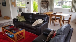 Una sala de estar con un sofá de cuero negro, una mesa de centro de madera y un tapete rojo. Hay un comedor con una mesa y sillas de madera.