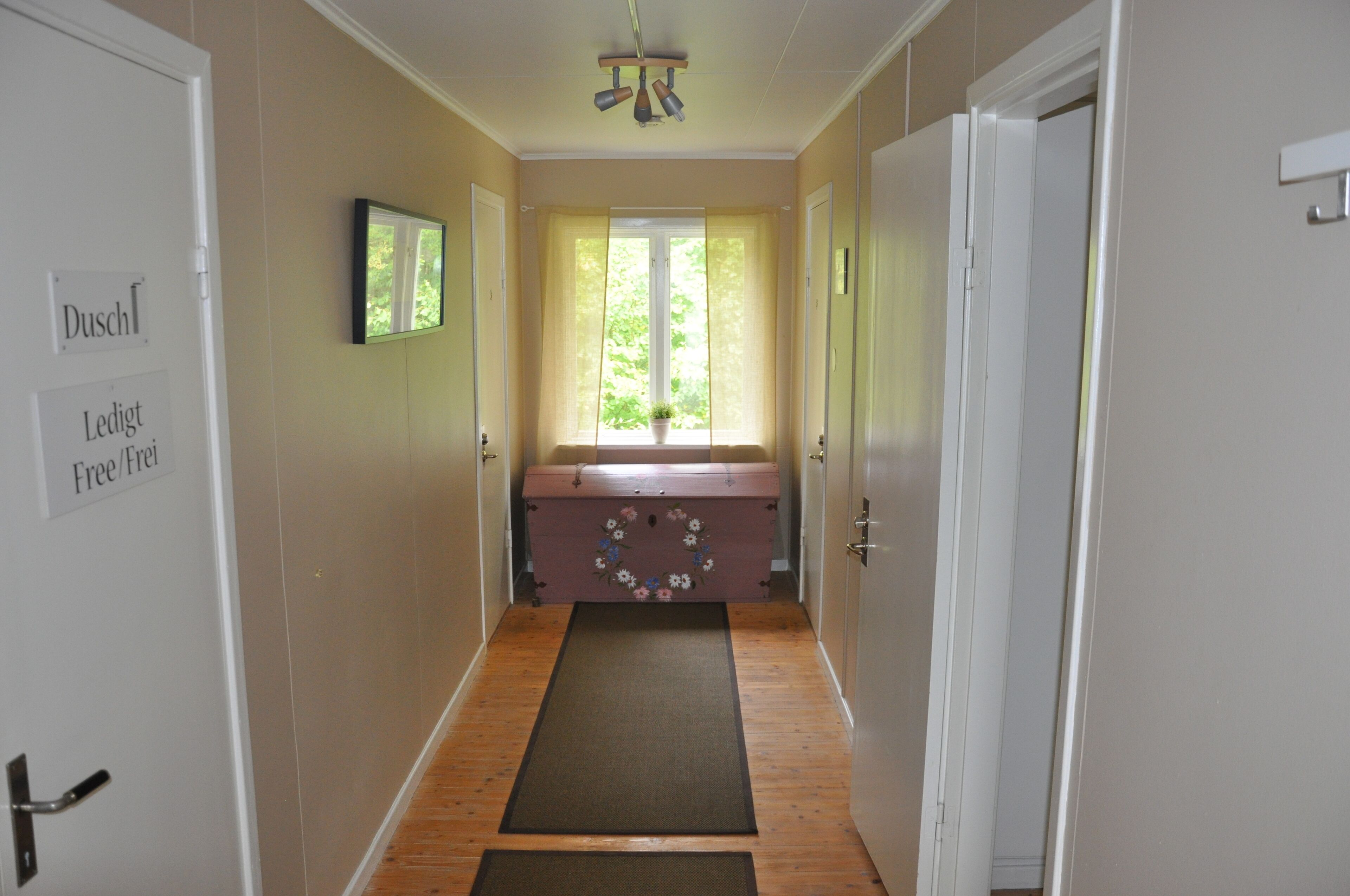 A hallway with a wooden floor, a bench with a floral design, a window with curtains, and a sign on the wall.