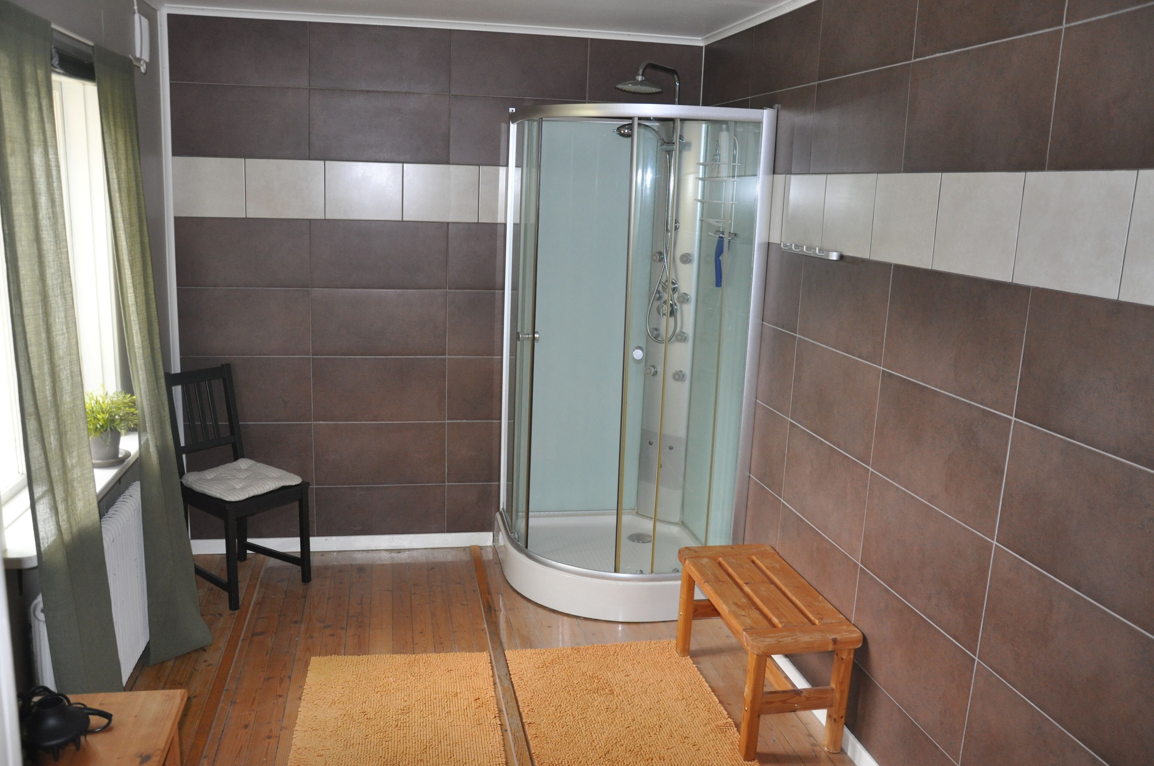 Une salle de bain avec une douche à parois de verre, un banc en bois, une plante en pot et un radiateur.