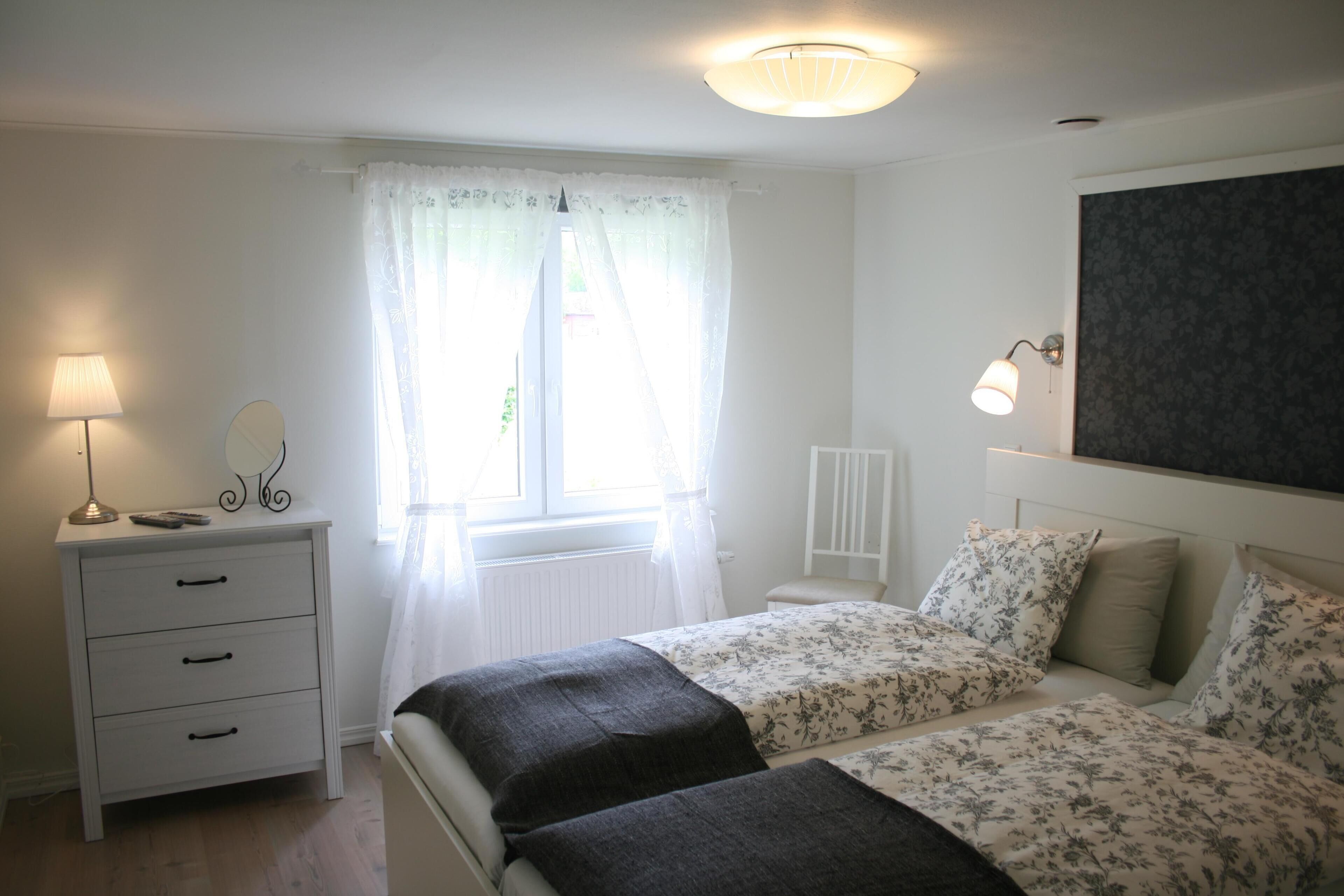 Een slaapkamer met twee bedden, een nachtkastje, een lamp, een spiegel en een raam met gordijnen.