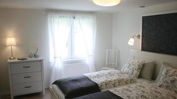 Een slaapkamer met twee bedden, een nachtkastje, een lamp, een spiegel en een raam met gordijnen.