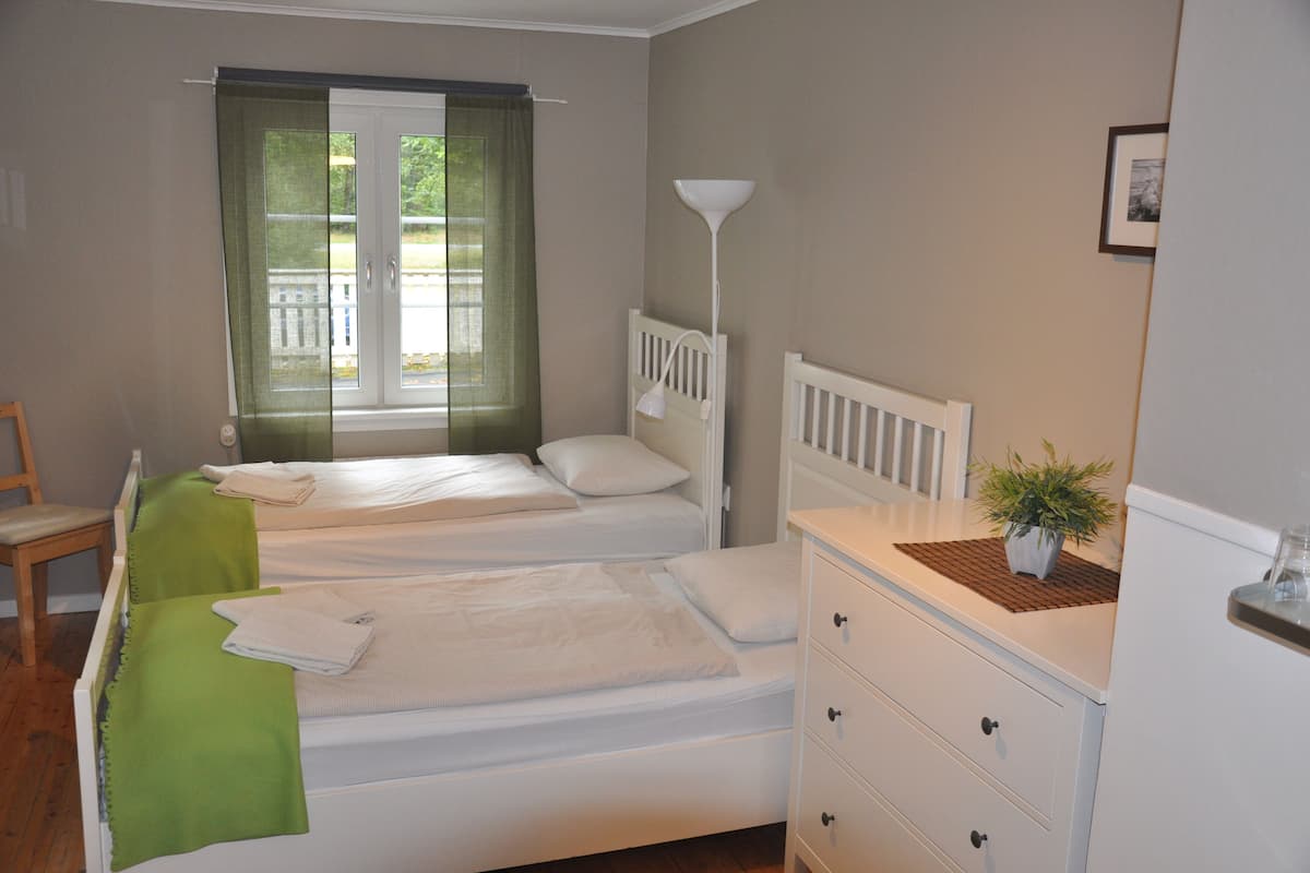 Une chambre avec deux lits, une table de chevet, une chaise, une fenêtre avec des rideaux et une lampe.