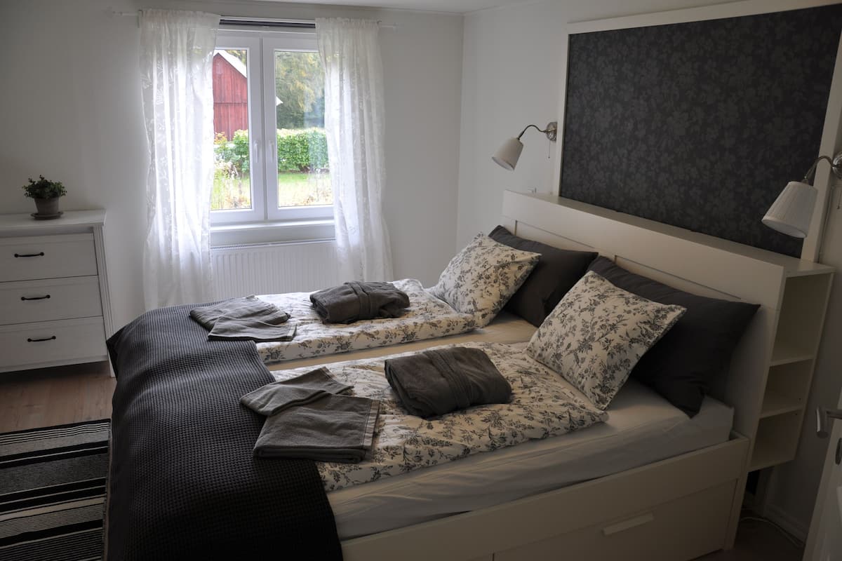Une chambre avec deux lits, une fenêtre avec des rideaux, une lampe de chevet et un radiateur.