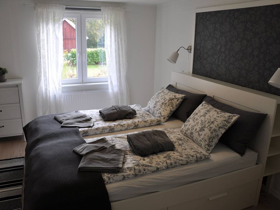 A bedroom with two beds, a window with curtains, a bedside lamp, and a radiator.