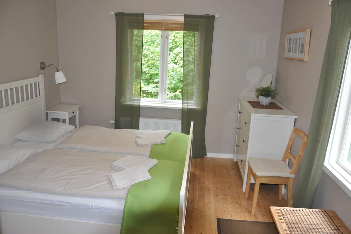 Une chambre avec deux lits, un bureau, une chaise, une fenêtre avec des rideaux et un radiateur.