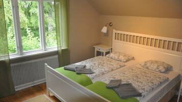 A bedroom with two single beds, a bedside table, a lamp, and a window with a view of greenery.