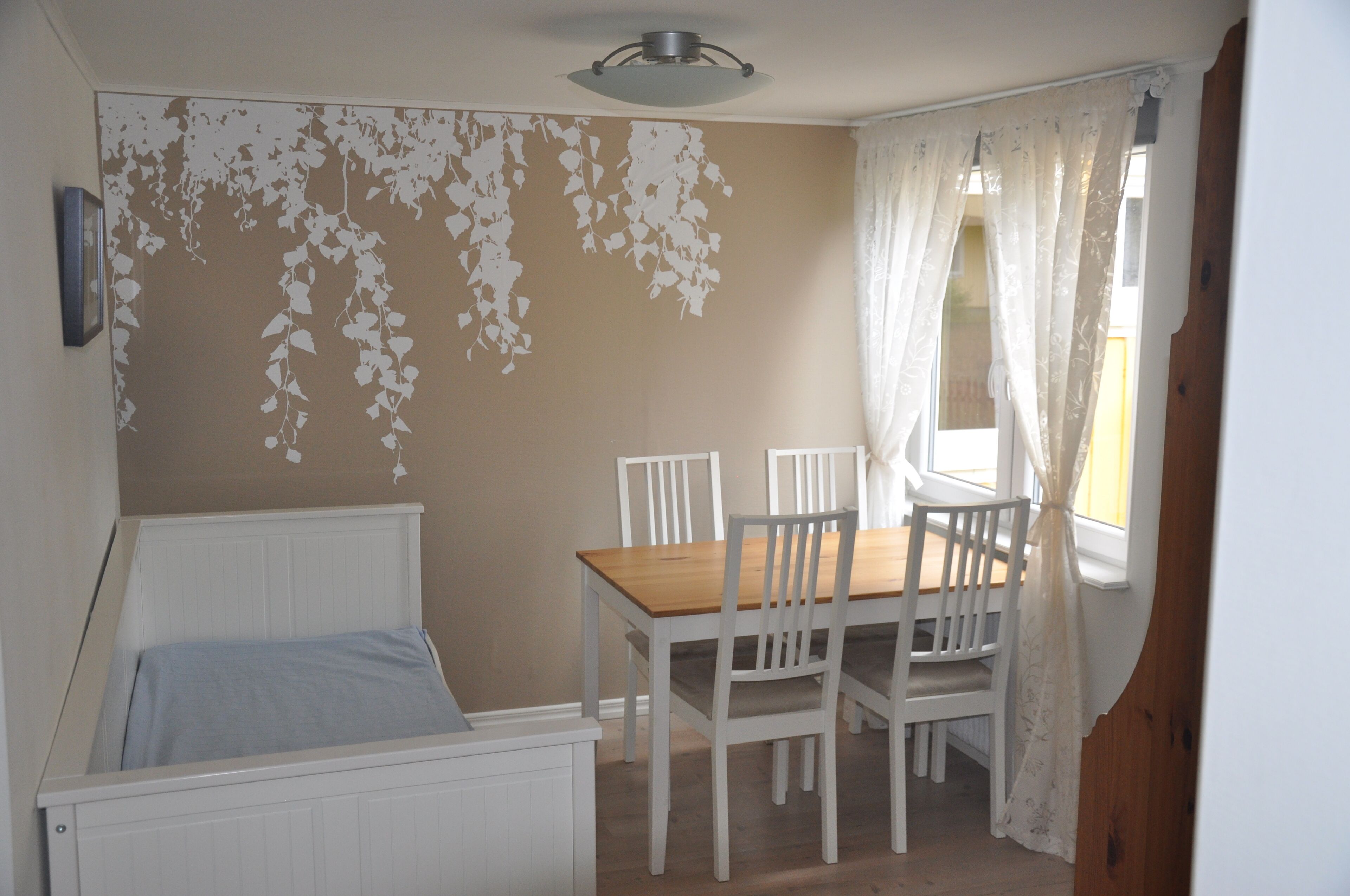 Un dormitorio con cama, una mesa con sillas, una ventana con cortinas y una pared con diseño de hojas.
