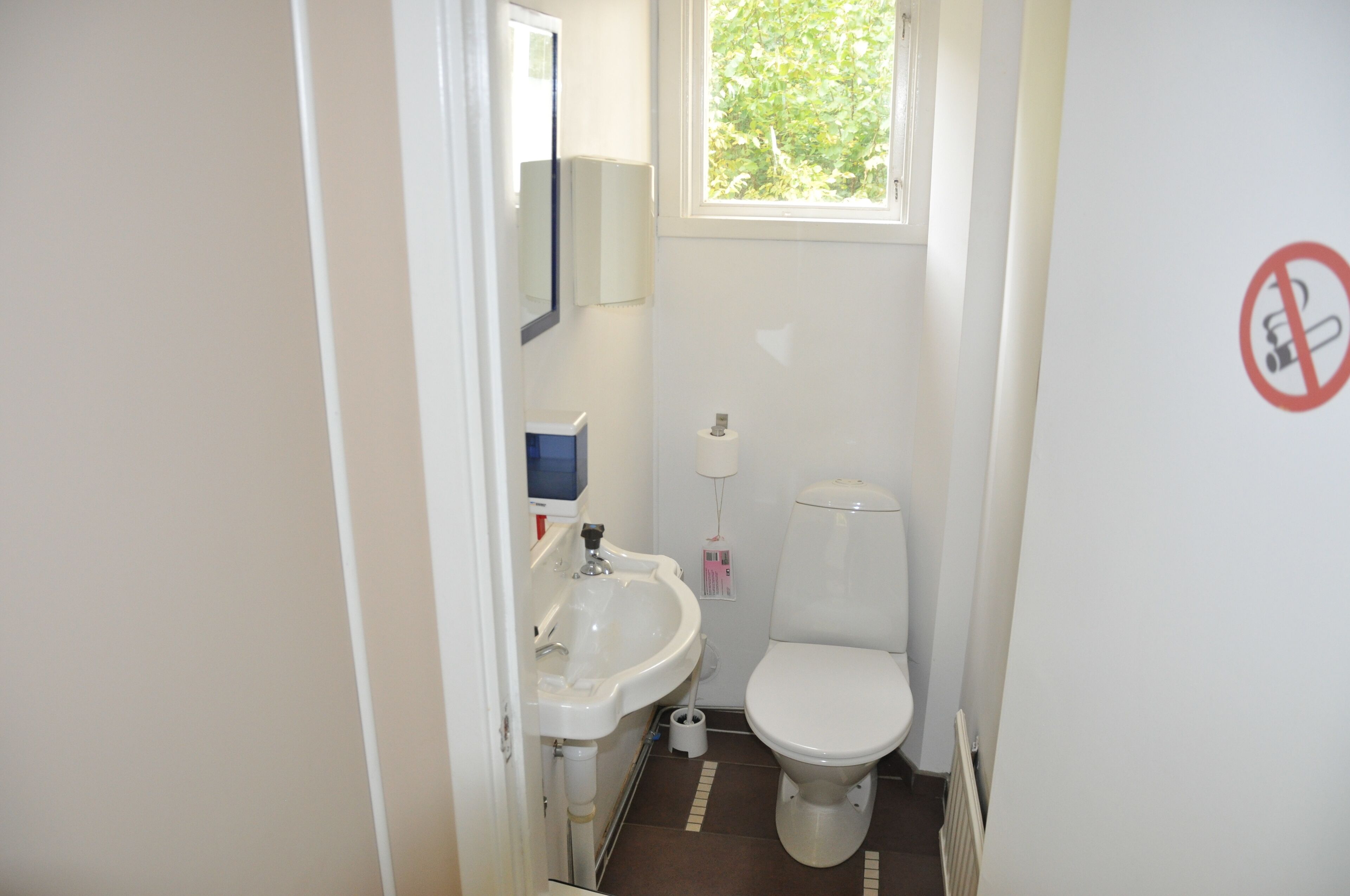 A small, compact bathroom with a white sink, toilet, and a window above the toilet.