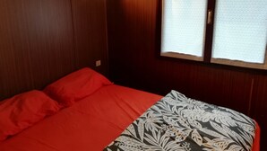 A room with a bed, wooden walls, a window with curtains, and a wall-mounted light. - Future is Nature Playground (Sala Biellese)