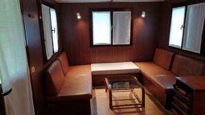 A compact, well-lit room with a sofa, a small table, and two windows with curtains. - Future is Nature Playground (Sala Biellese)