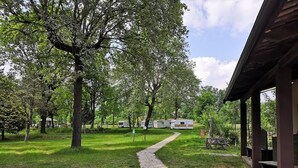 A campground with a gravel path leading to RVs, surrounded by trees and a covered pavilion. - Future is Nature Playground (Sala Biellese)