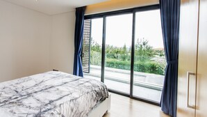 Et moderne soveværelse med en stor seng, en skydedør til en balkon og udsigt til grøn natur.