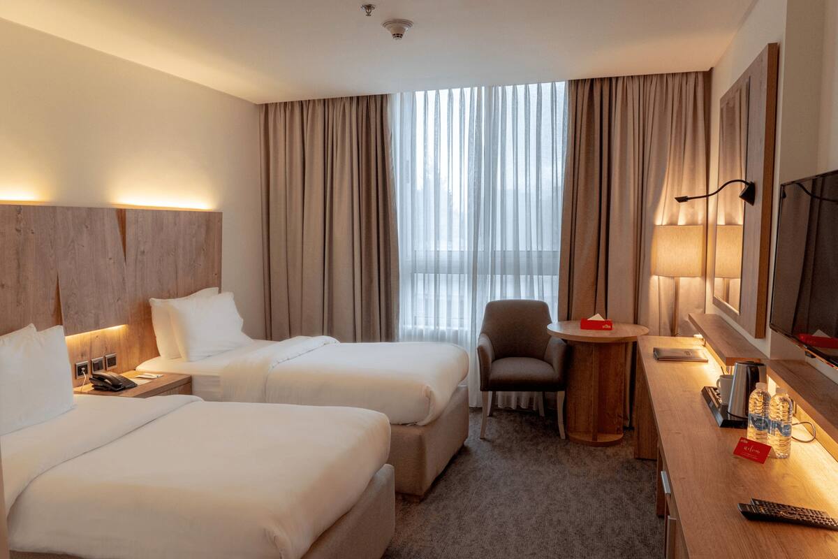 Ein Hotelzimmer mit zwei Betten, einem Schreibtisch, einem Stuhl, einem Fernseher und einem Fenster mit Vorhängen.