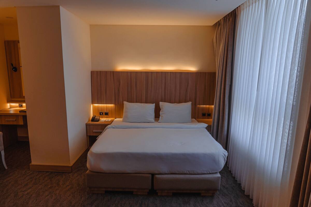 Ein Hotelzimmer mit einem großen Bett, Nachttischlampen, einem Schreibtisch und einem Fenster mit Vorhängen.