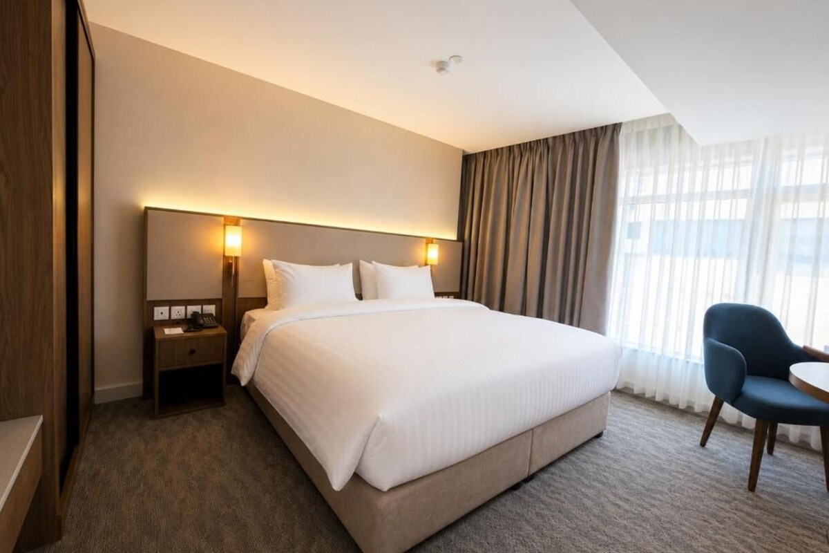 Een hotelkamer met een groot bed, nachtkastjes, een stoel en een raam met gordijnen.