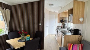 Cocina compacta con estufa, lavaplatos y microondas. Hay un comedor con mesa y sillas, además de un sofá con un cojín colorido.
