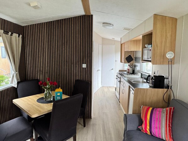 Cocina compacta con estufa, lavaplatos y microondas. Hay un comedor con mesa y sillas, además de un sofá con un cojín colorido.