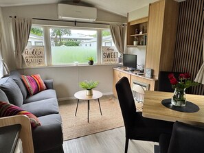 Una sala de estar moderna con un sofá gris, una mesita redonda con una planta y un comedor con una mesa y sillas de madera.