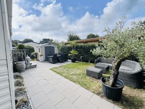 Un patio con mobiliario exterior, un cobertizo y un pequeño jardín.