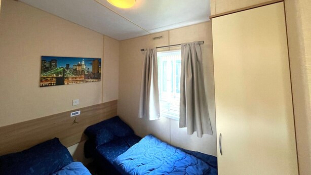 A room with two beds, a window with curtains, a wall-mounted picture, and a ceiling light. - KD 814 - Vakantiepark Kijkduin (Den Haag)