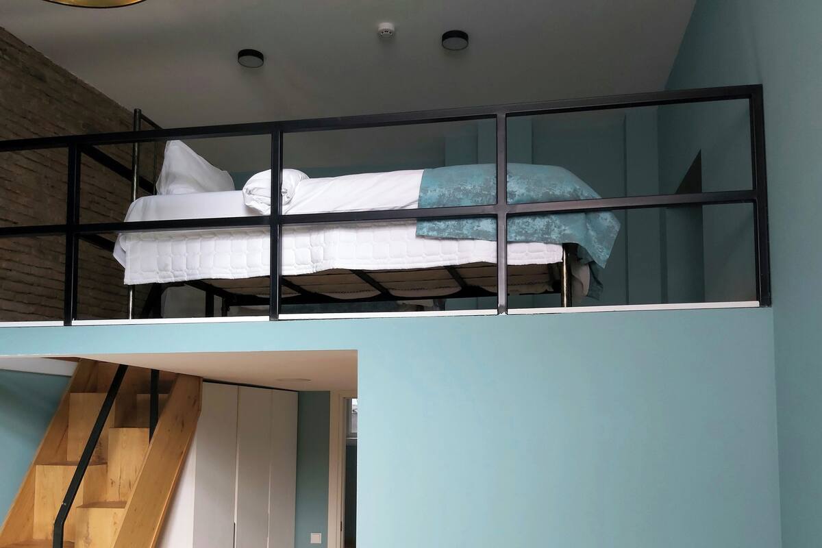 A bunk bed with a mattress and pillows, a wooden staircase, and a light blue wall.