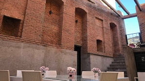 A courtyard with brick walls, a glass table, and wicker chairs. - History of Tbilisi (Tbilisi)