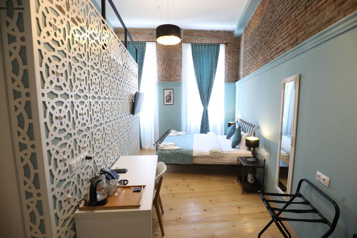 A room with a bed, a desk, a chair, a mirror, and a decorative wall panel.