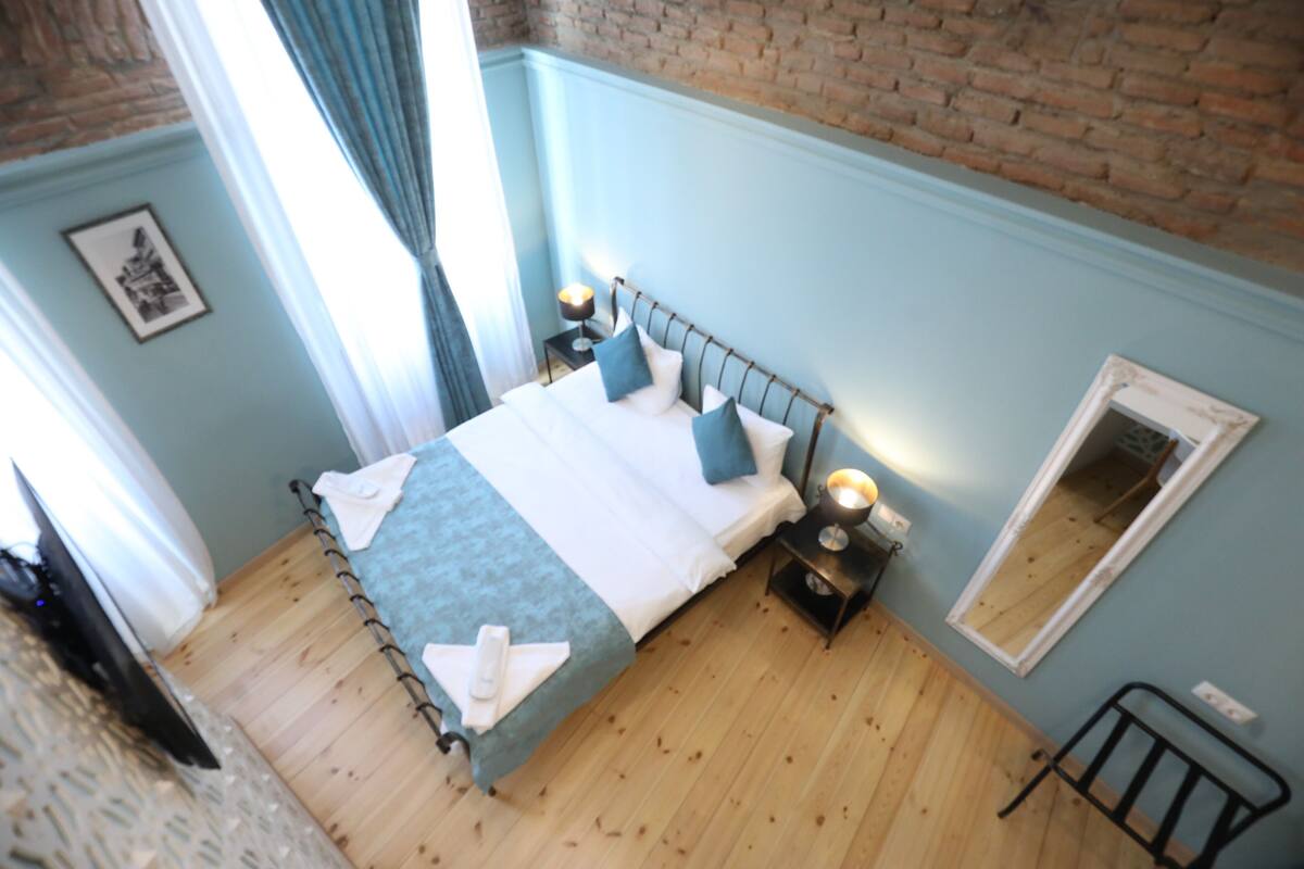 A bedroom with a bed, bedside tables, a mirror, and a brick wall.