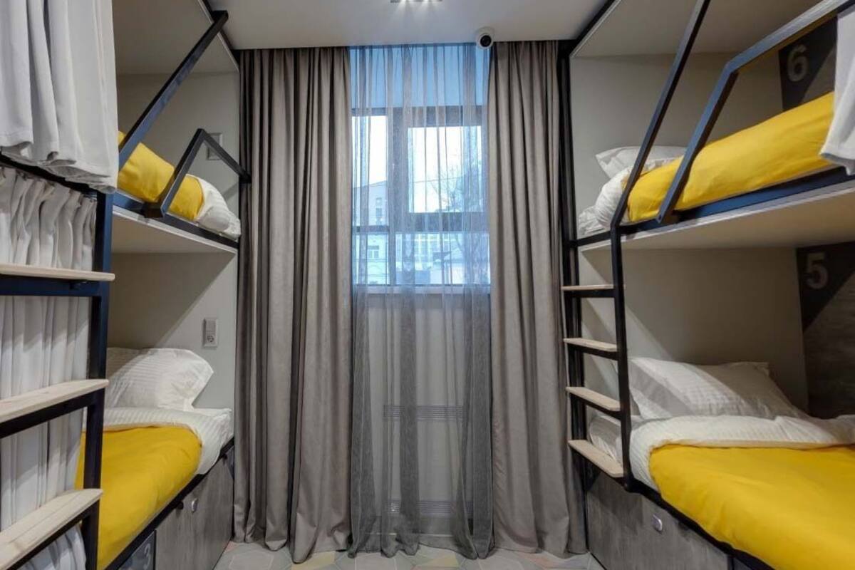 Une chambre de dortoir avec des lits superposés, une fenêtre avec des rideaux et un luminaire au plafond.