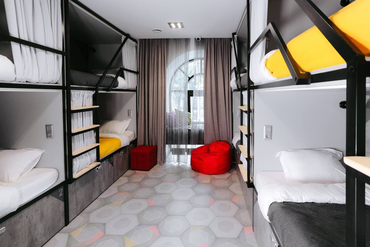 Une chambre d’hôtel compacte avec des lits superposés, un fauteuil en forme de sac de haricots rouge et une vue dégagée sur l’extérieur grâce à une grande fenêtre.