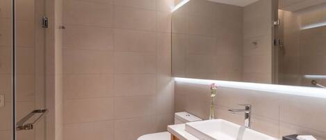 A modern bathroom with a white sink, a large mirror, and a toilet.