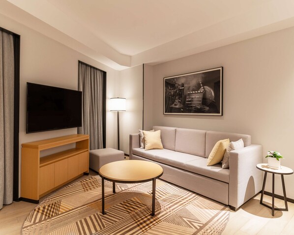 A modern living room with a flat-screen TV, a sofa, a small round table, a lamp, and a framed picture on the wall. - Hyatt Place Changchun Jingyue (Changchun)